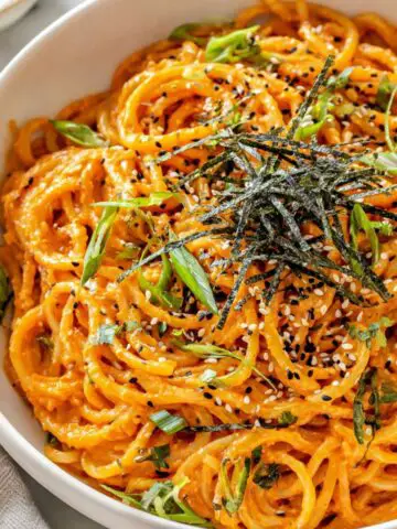 Gochujang pasta served in a bowl with garnishes on a white kitchen counter.