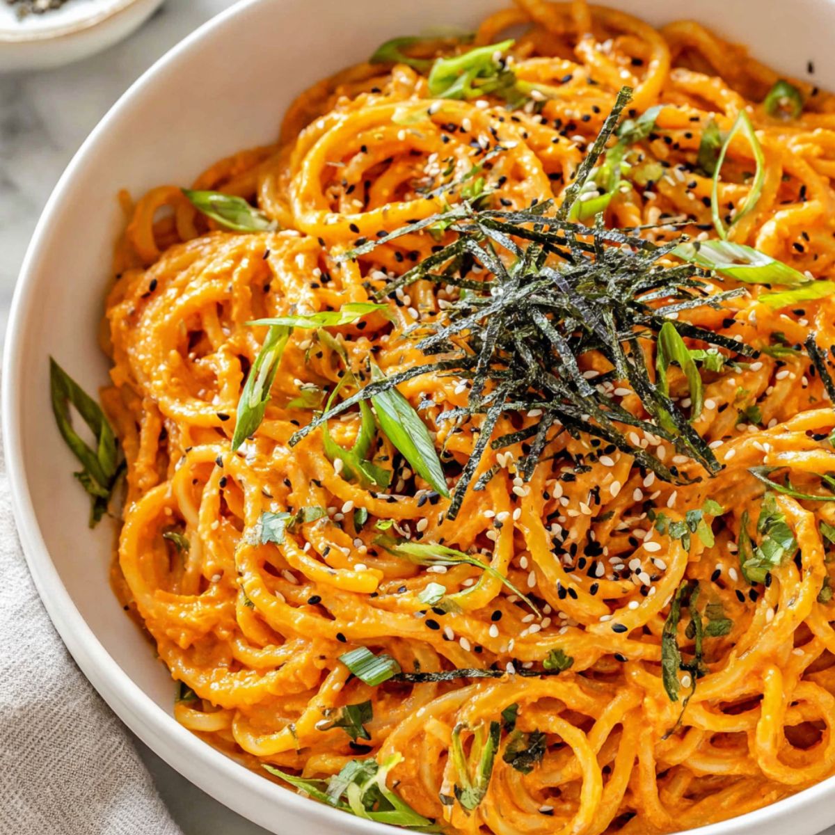 Gochujang pasta served in a bowl with garnishes on a white kitchen counter.