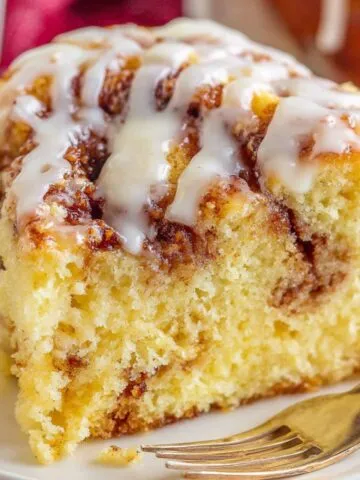 A slice of Cinnamon roll cake mix with icing drizzle on a white plate