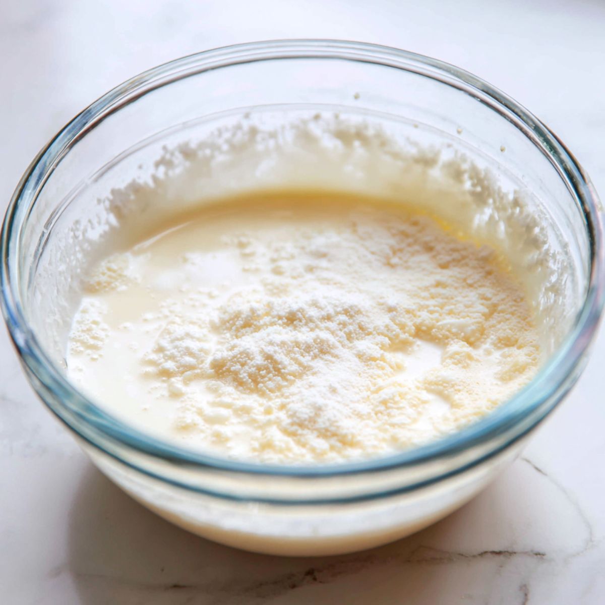 Milk mochi batter being mixed in a bowl on a white kitchen counter