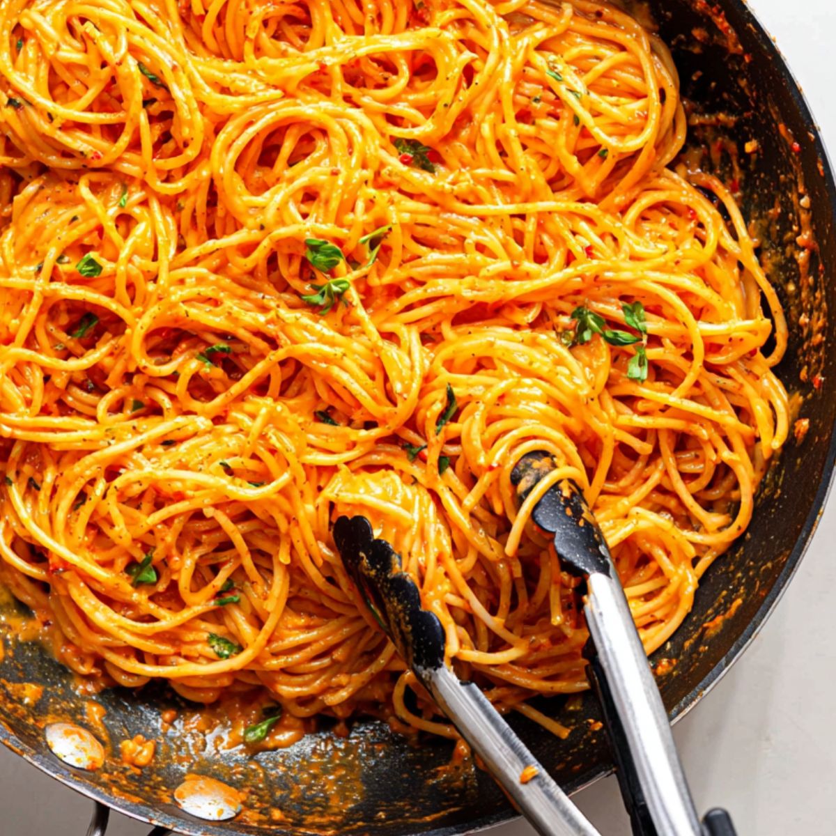 Pasta being tossed in gochujang sauce with garnishes on the side.