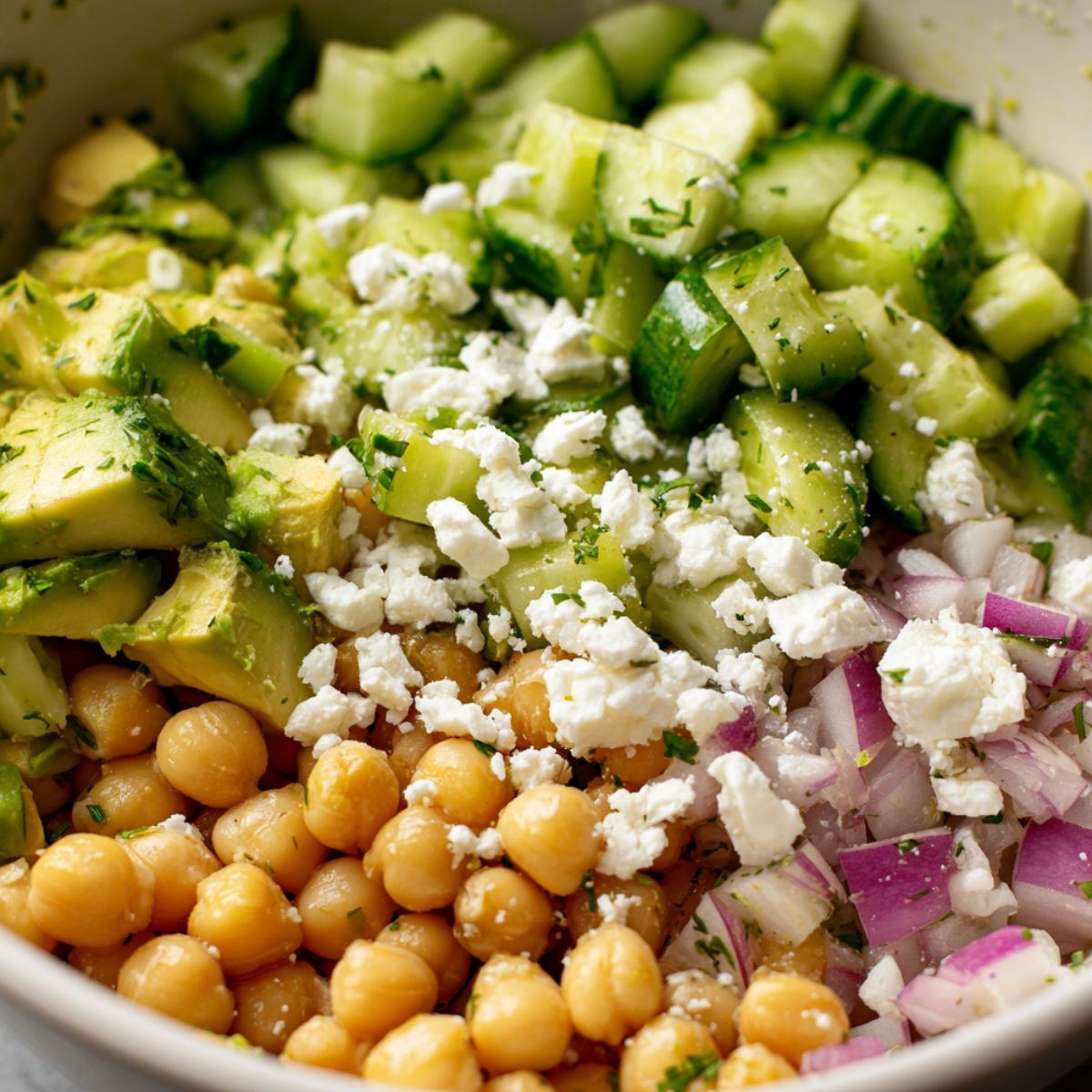 Tossing chickpeas, avocado, and feta together in a mixing bowl