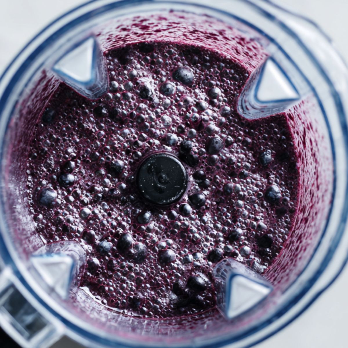 Blending healthy blueberry smoothie in a blender on a white kitchen counter