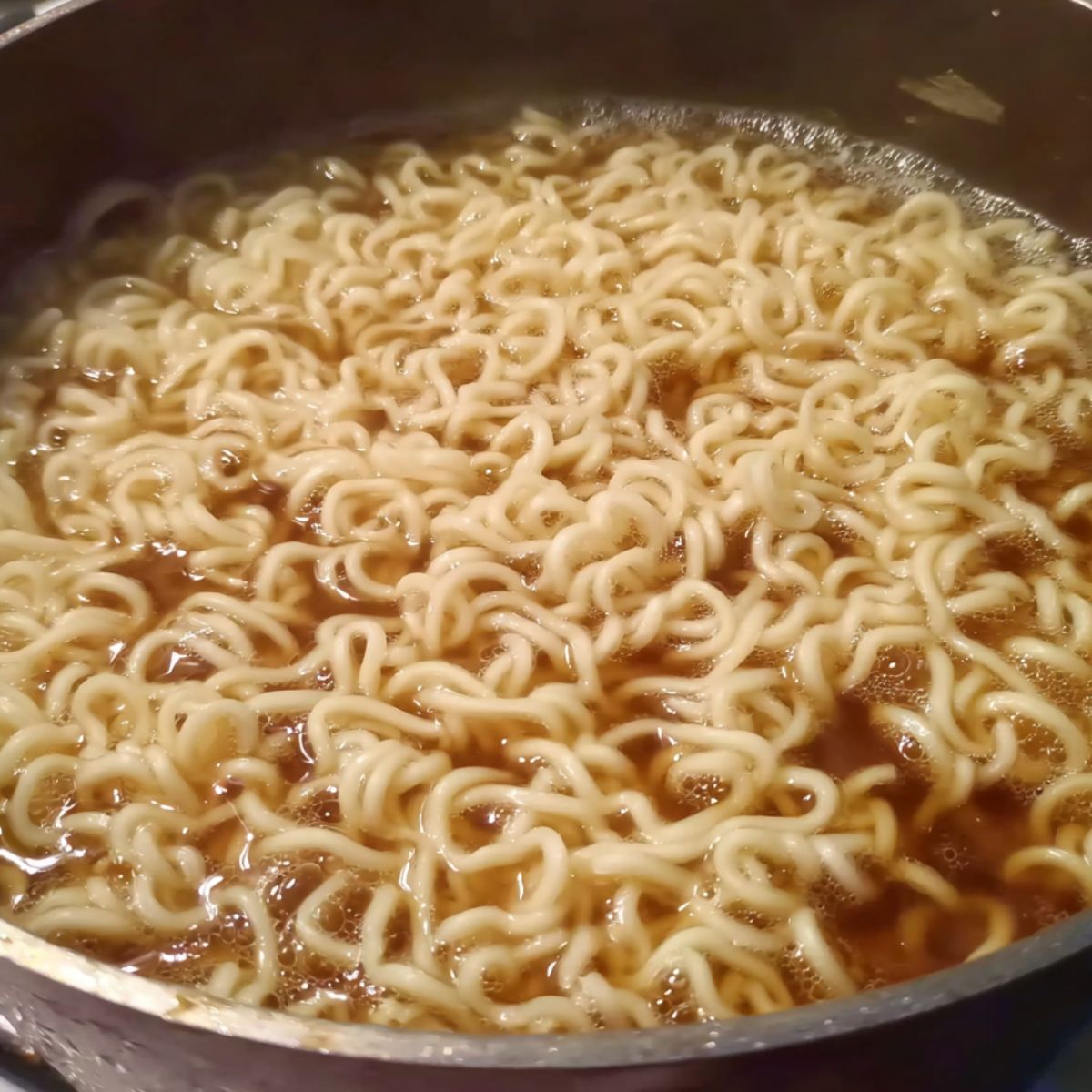 Ramen noodles boiling in a small pot on a stove.
