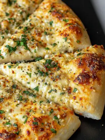 Freshly baked cheesy garlic pizza on a white kitchen counter with golden crust and bubbling cheese