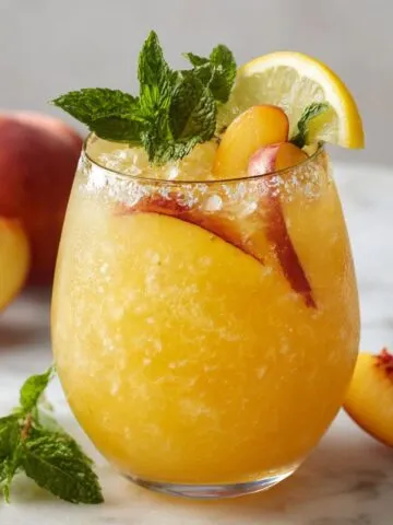Frozen beach peach lemonade served in a glass with peach and lemon garnish