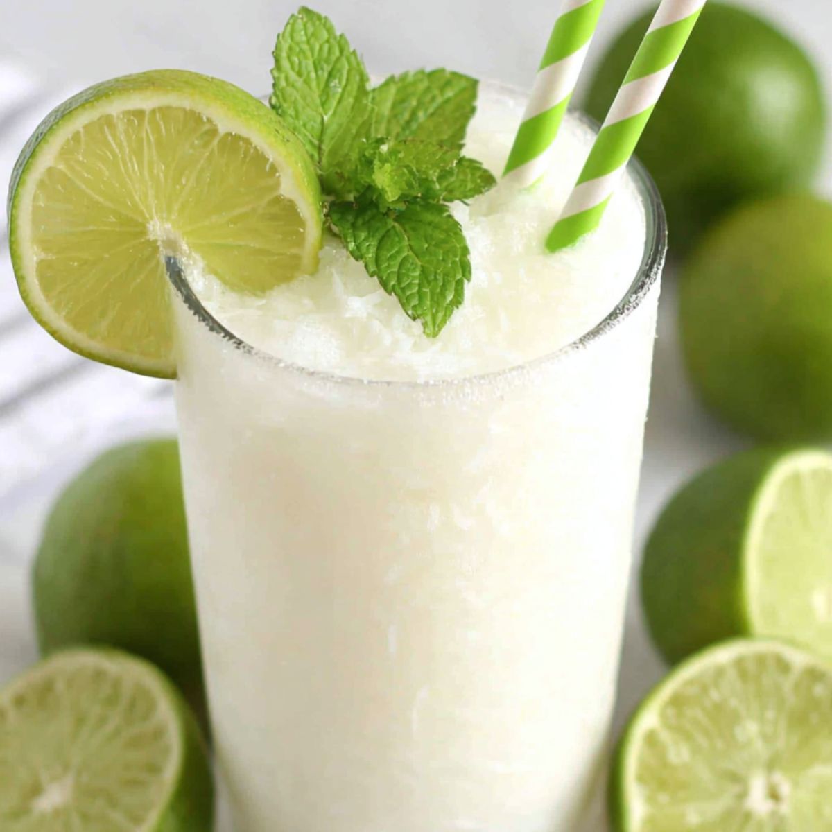 A glass of homemade coconut limeade with lime slices and mint on a white kitchen counter