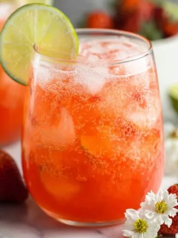 Homemade strawberry limeade in a glass with fresh fruit on a kitchen counter