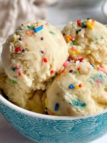 Homemade edible sugar cookie dough scooped into a small white bowl with sprinkles on top