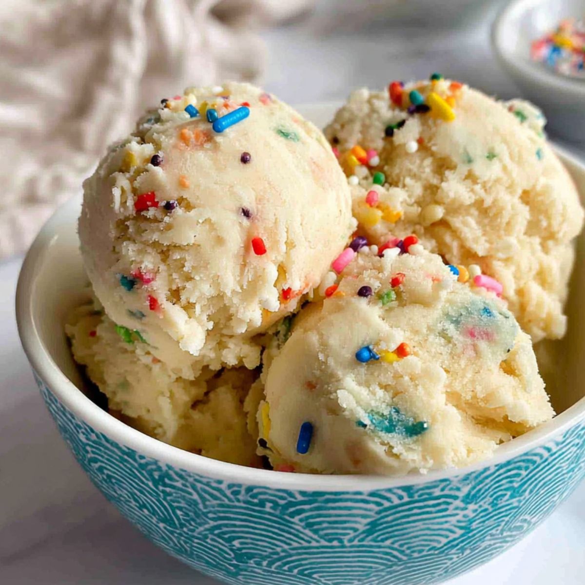 Homemade edible sugar cookie dough scooped into a small white bowl with sprinkles on top