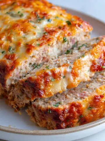 Sliced chicken cordon bleu meatloaf on a white plate, cheese melting out