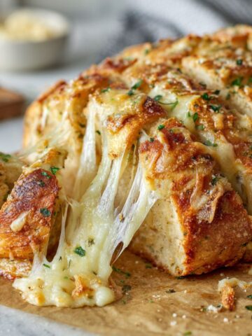 Homemade stuffed cheesy bread with golden crust and melted cheese pulls on a white kitchen counter