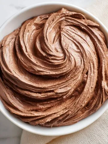 Whipped Chocolate Cream Recipe in a bowl, swirled with soft, fluffy peaks on a kitchen counter.