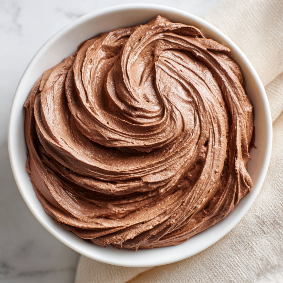 Whipped Chocolate Cream Recipe in a bowl, swirled with soft, fluffy peaks on a kitchen counter.