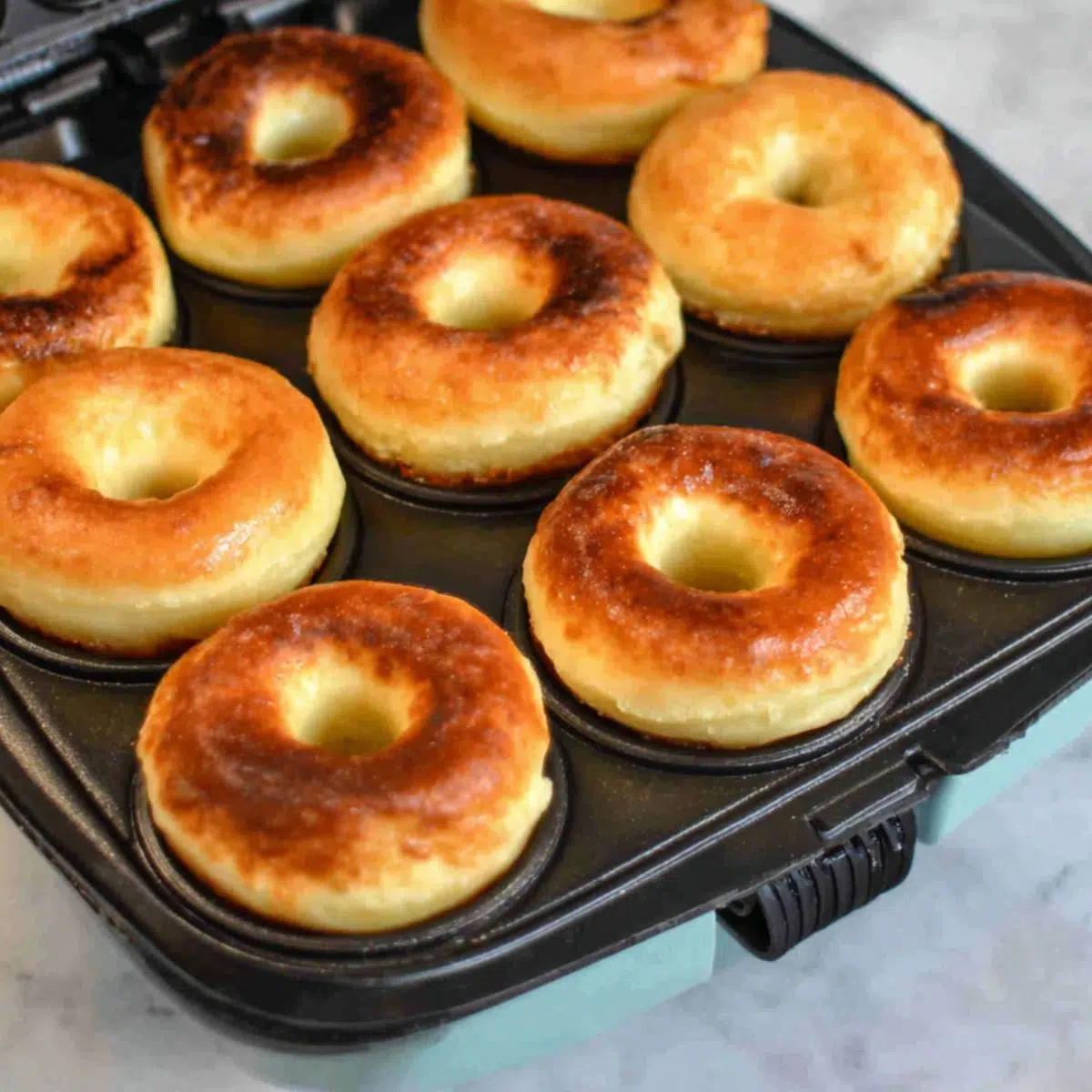 Piping donut batter into a mini donut maker on a white kitchen counter