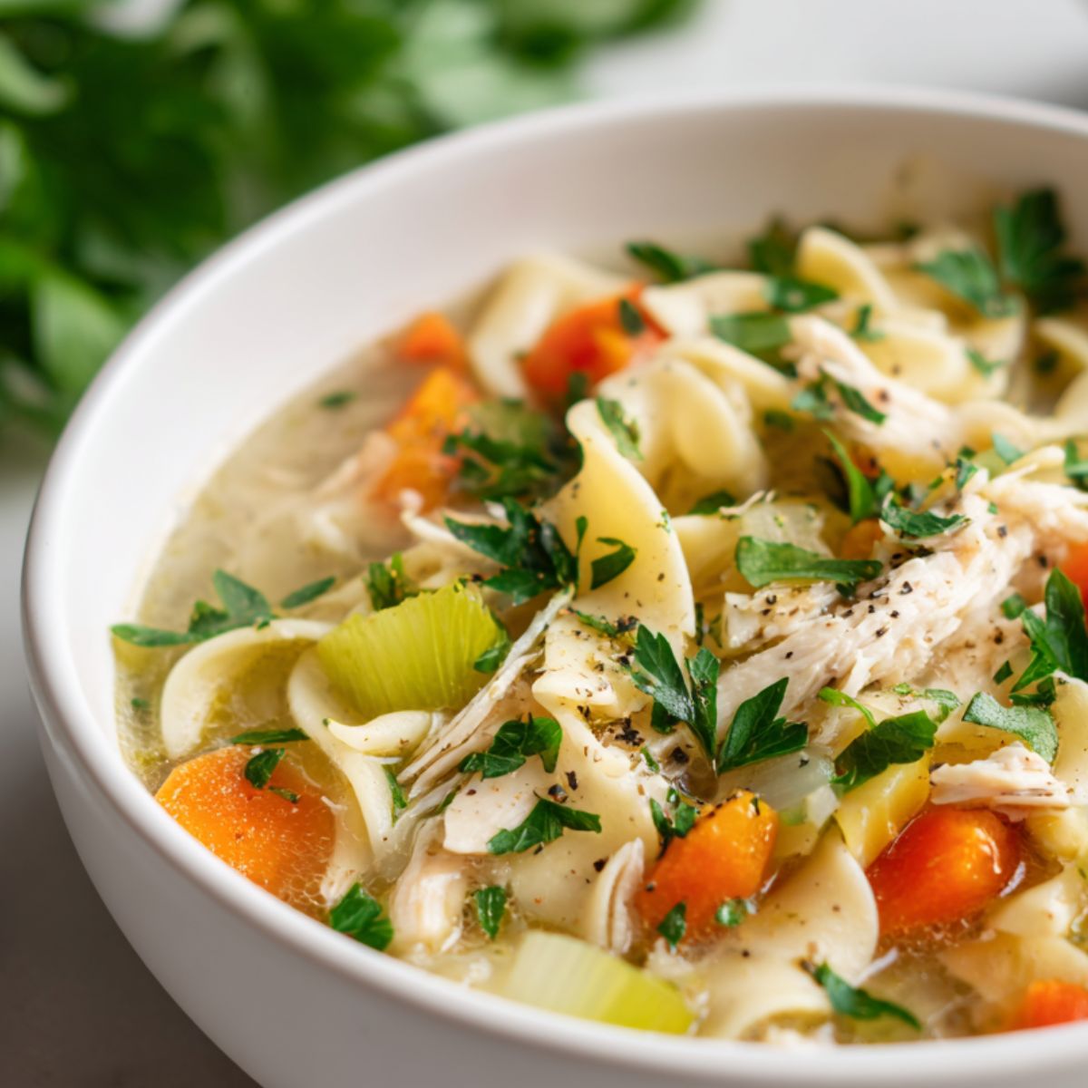 Homemade gluten-free chicken noodle soup served in a ceramic bowl on a white kitchen counter