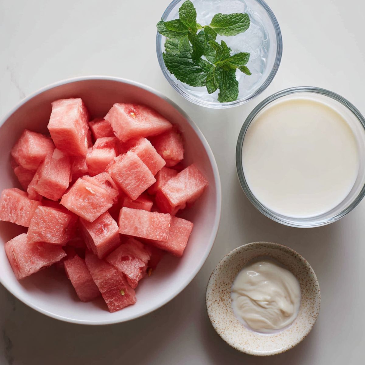 Ingredients for Hwachae bowl on a white counter: cubed watermelon, Sprite bottle, milk, condensed milk