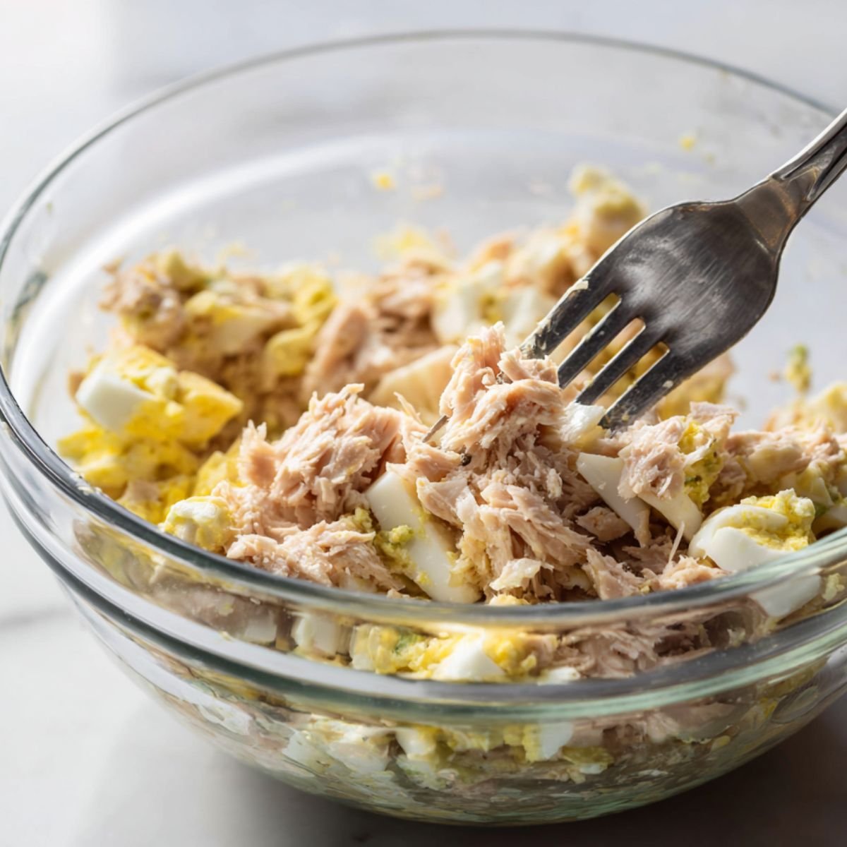 Bowl of flaked tuna and chopped eggs being gently combined with a fork