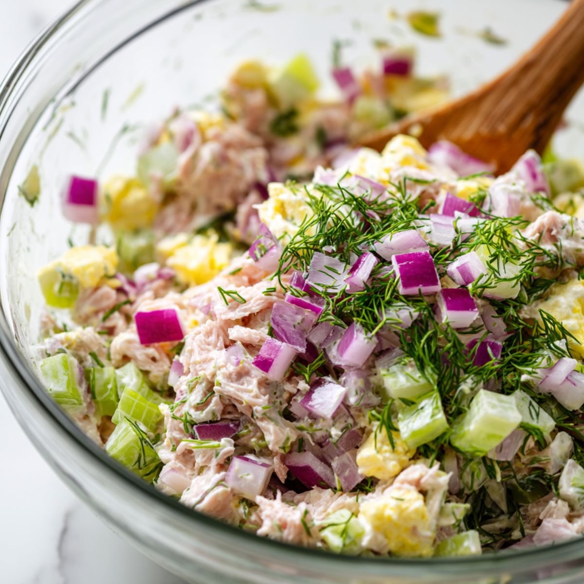 Adding celery, red onion, and dill to tuna salad mixture in a bowl