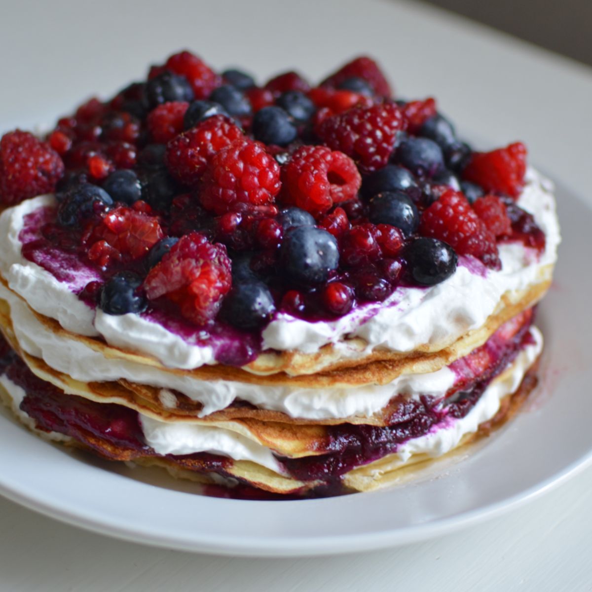 Layering pancake cake with cream and berries