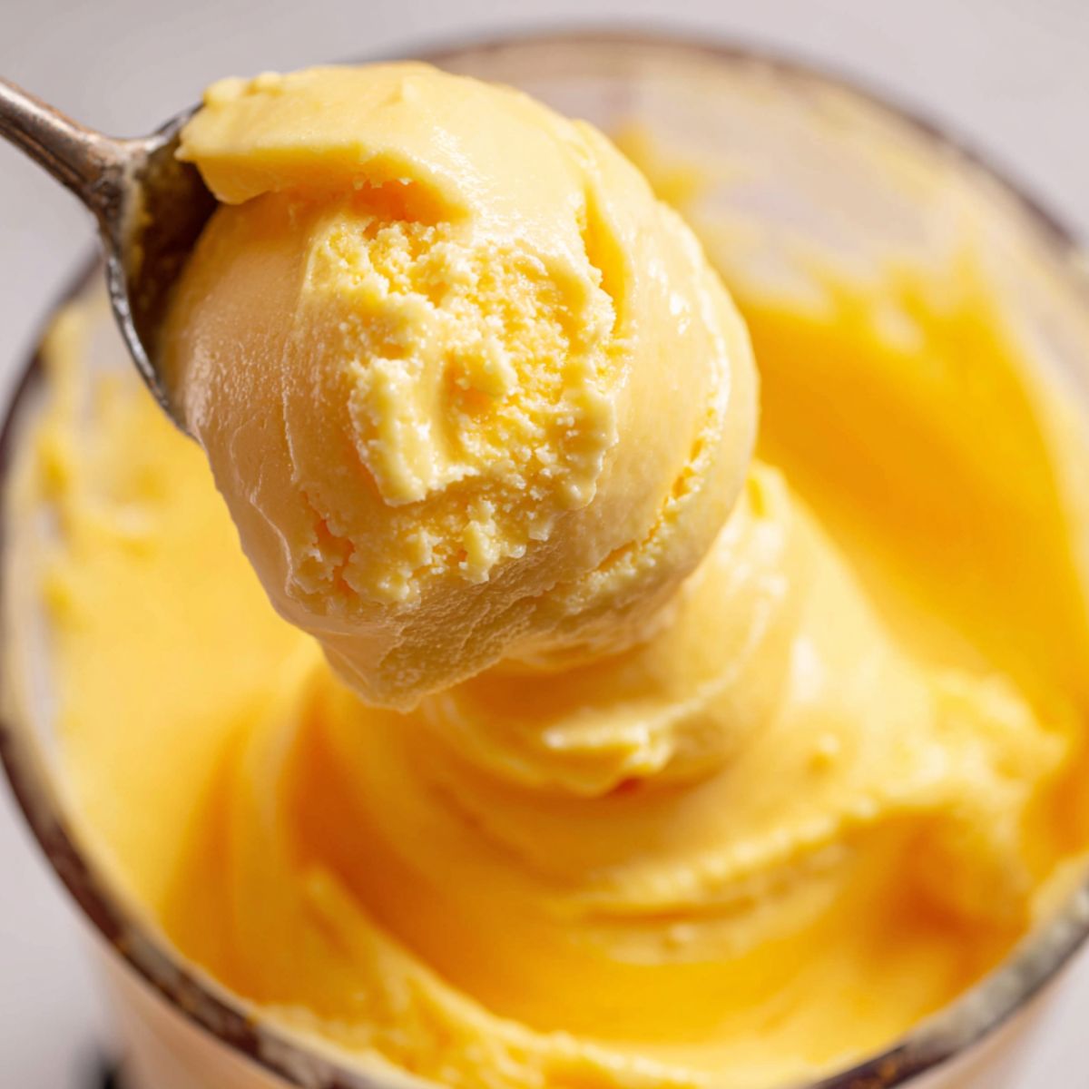 Spoon lifting smooth mango sorbet from blender showing texture
