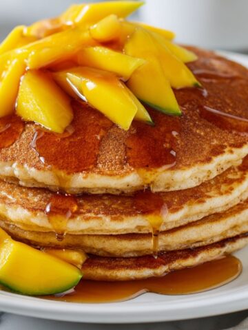 Fluffy homemade mango pancakes stacked on a plate on a white kitchen counter.