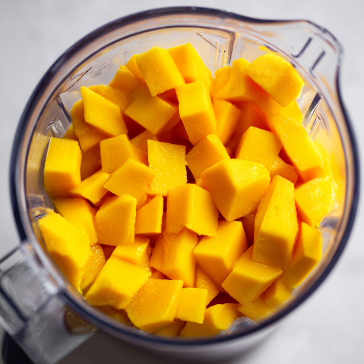 Diced mango pieces being blended into puree on a white counter.