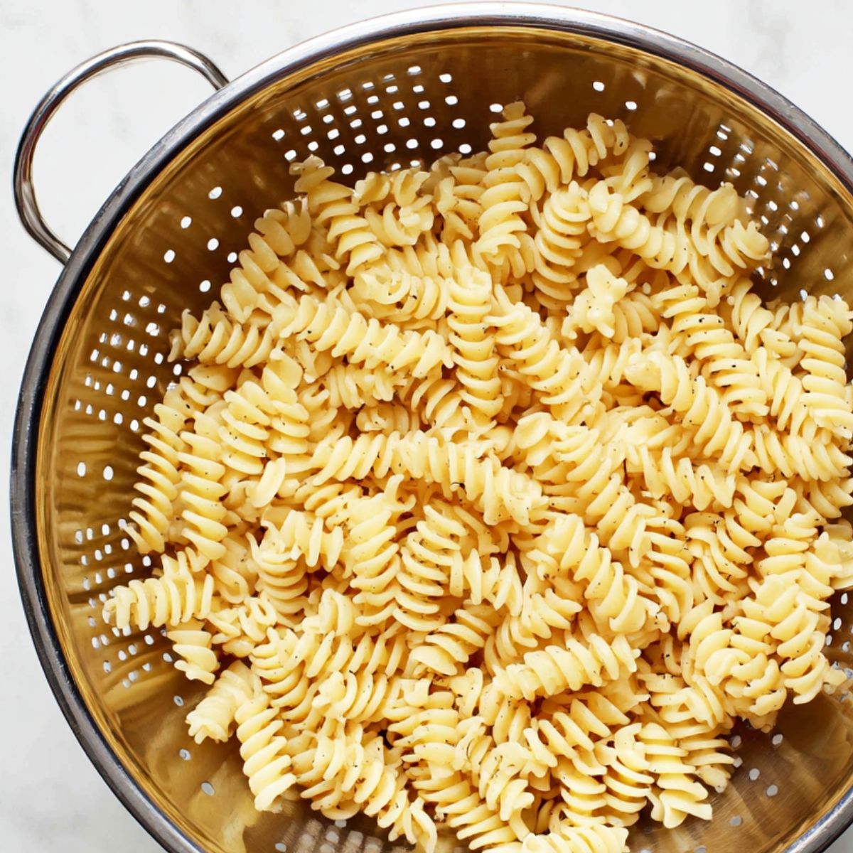 Draining freshly cooked rotini pasta in a colander