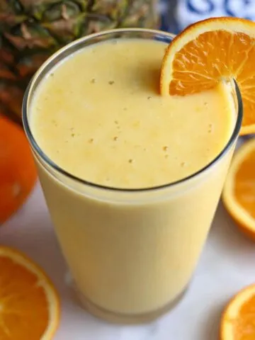 Pineapple orange smoothie served on a kitchen counter with fresh fruit