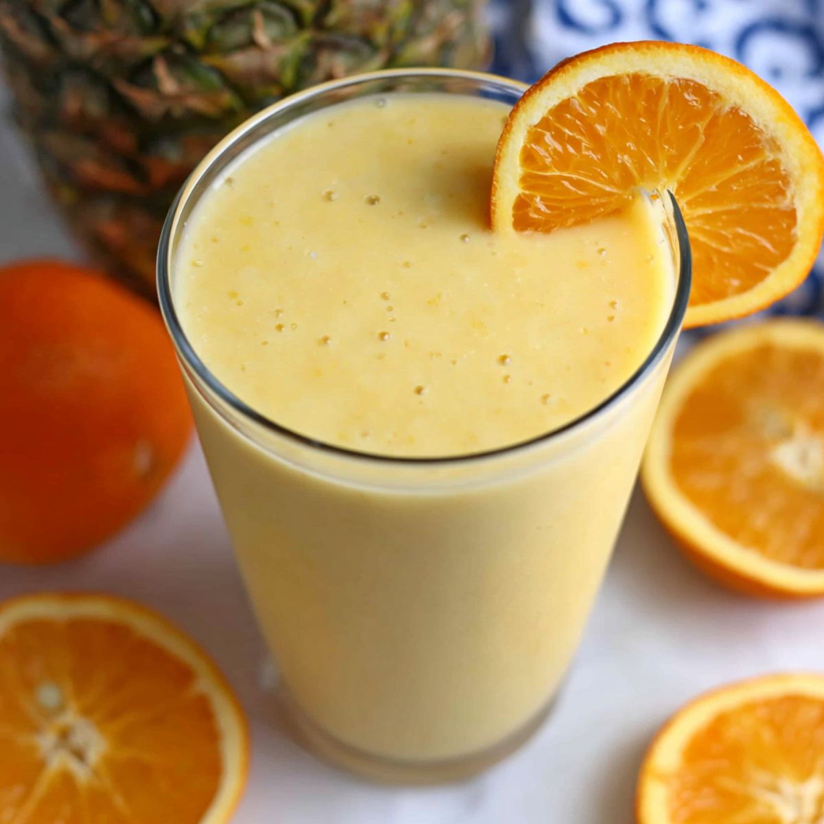 Pineapple orange smoothie served on a kitchen counter with fresh fruit