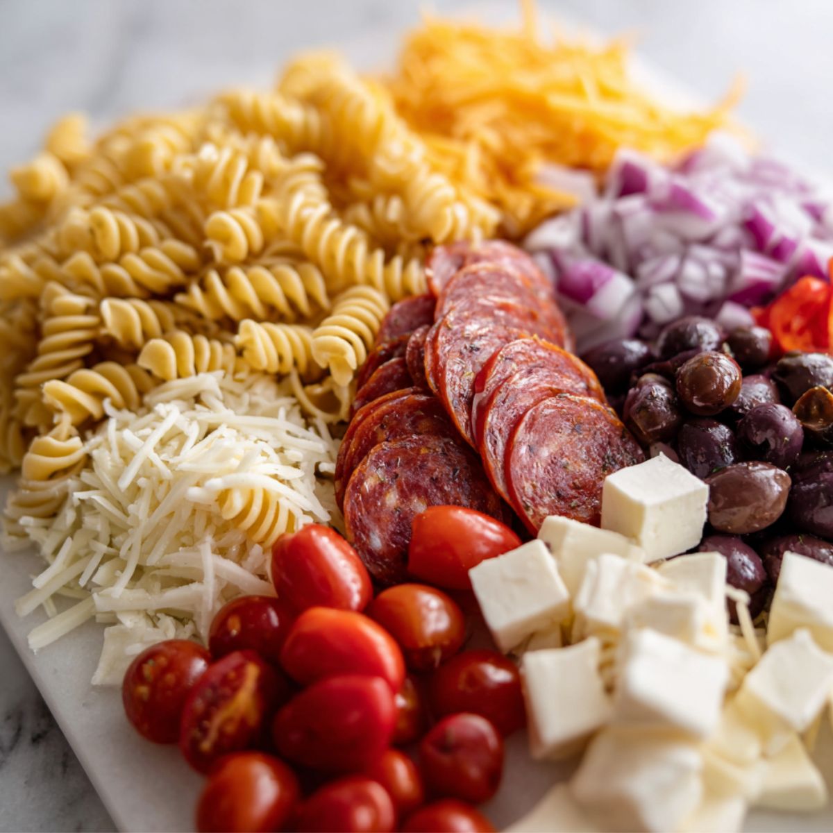 Ingredients for pizza pasta salad on a white counter before prep