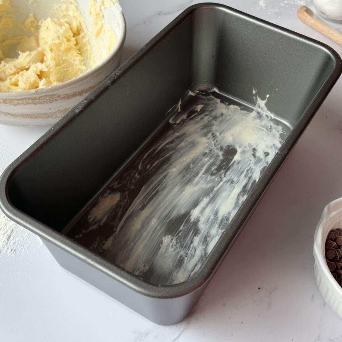 Mashed bananas and greased loaf pan on a white counter