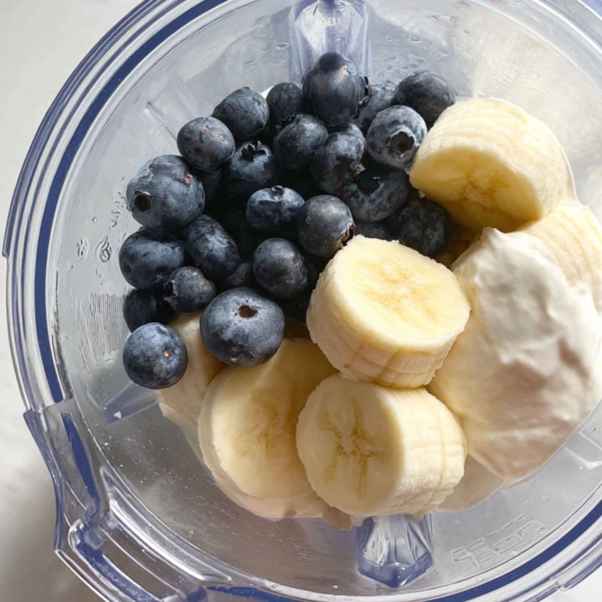 Layering ingredients into a blender for blueberry smoothie preparation