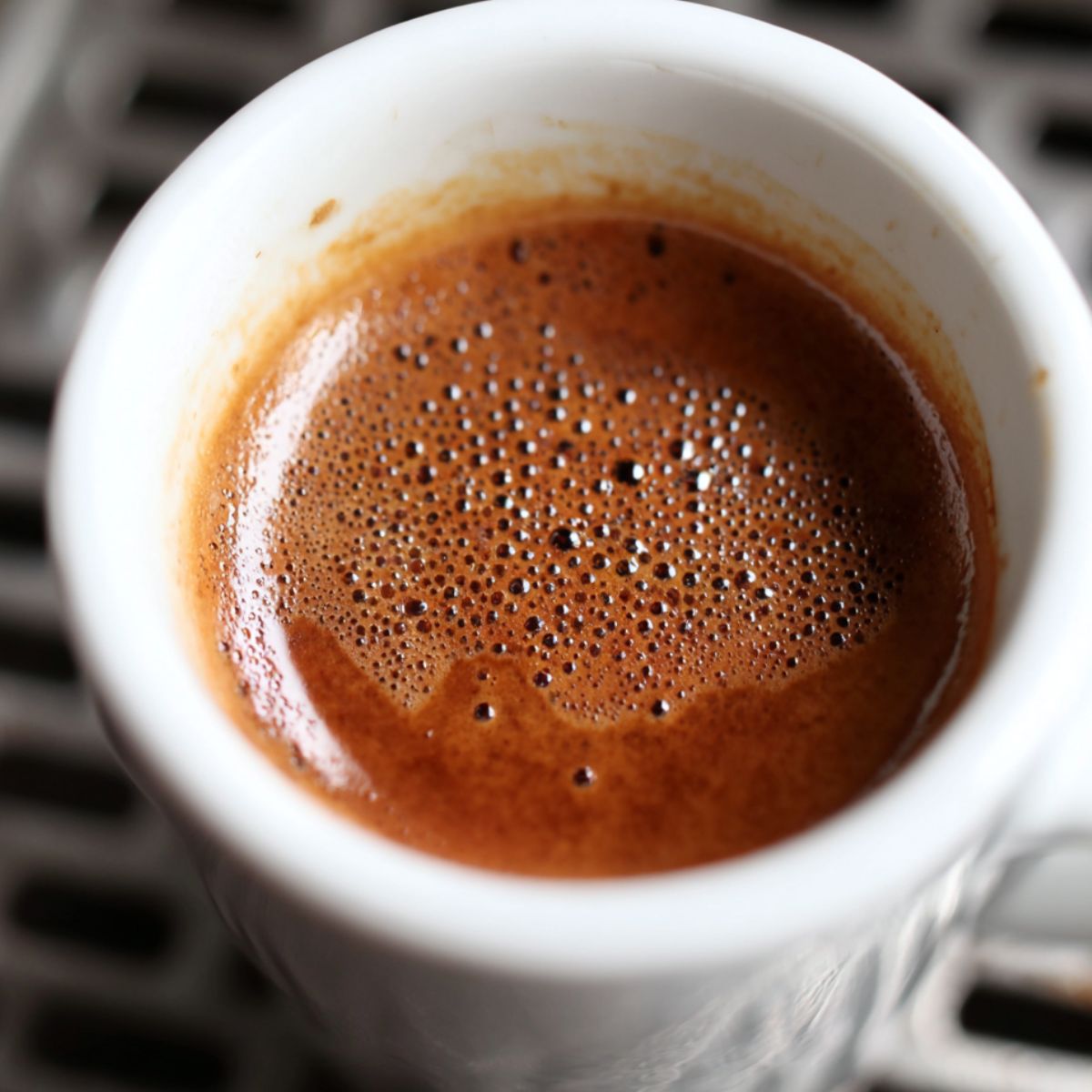 Freshly brewed espresso shot on a white counter beside a moka pot.