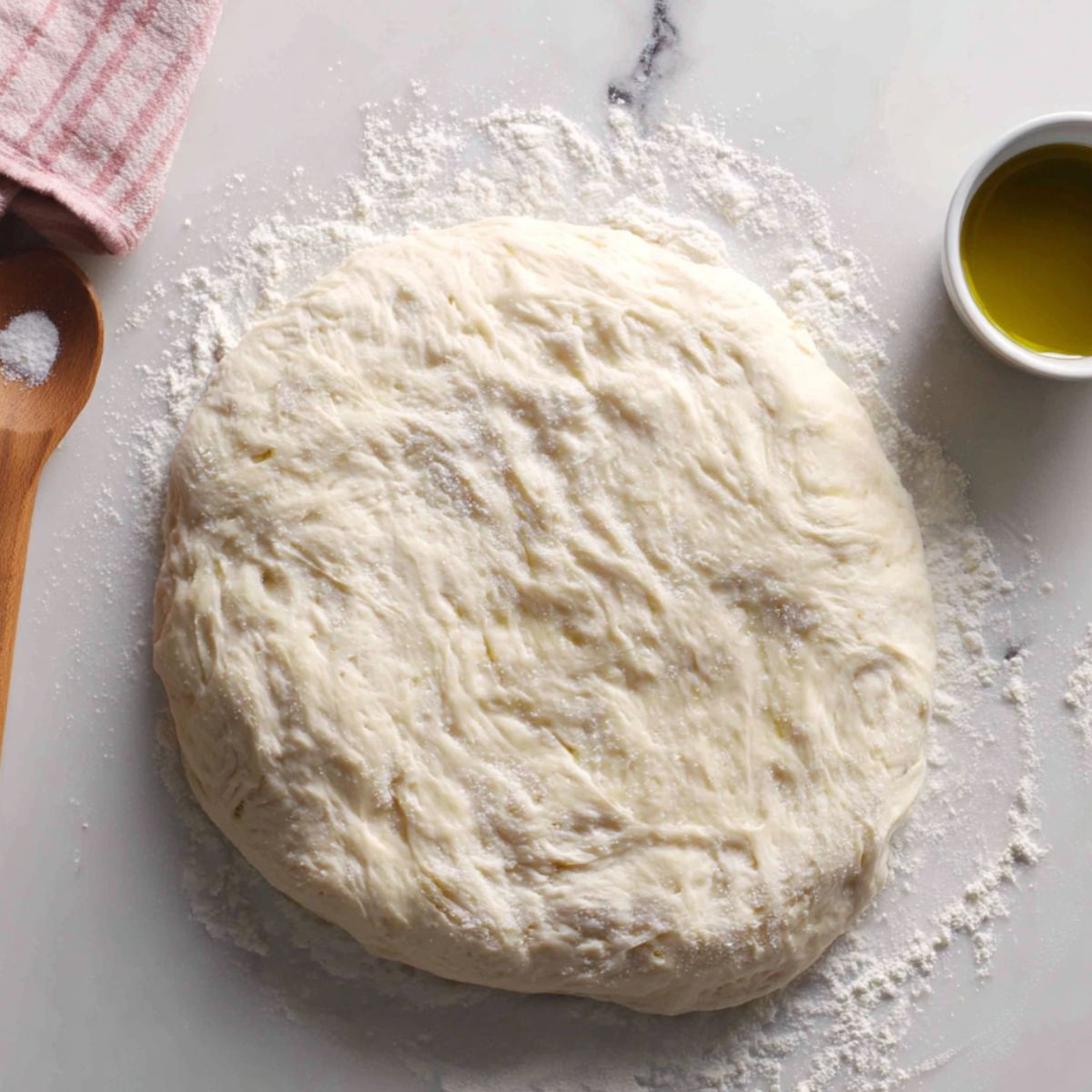 Rolled-out pizza dough brushed with olive oil and sprinkled with salt on a floured counter