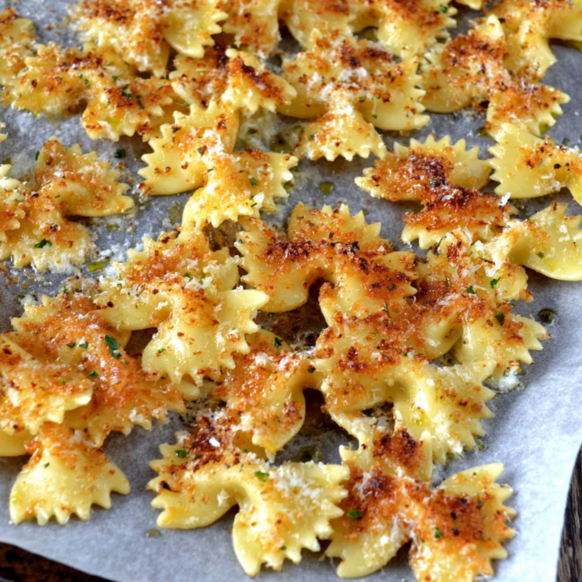 Pasta chips mid-bake on a parchment-lined baking tray, some edges golden and curling