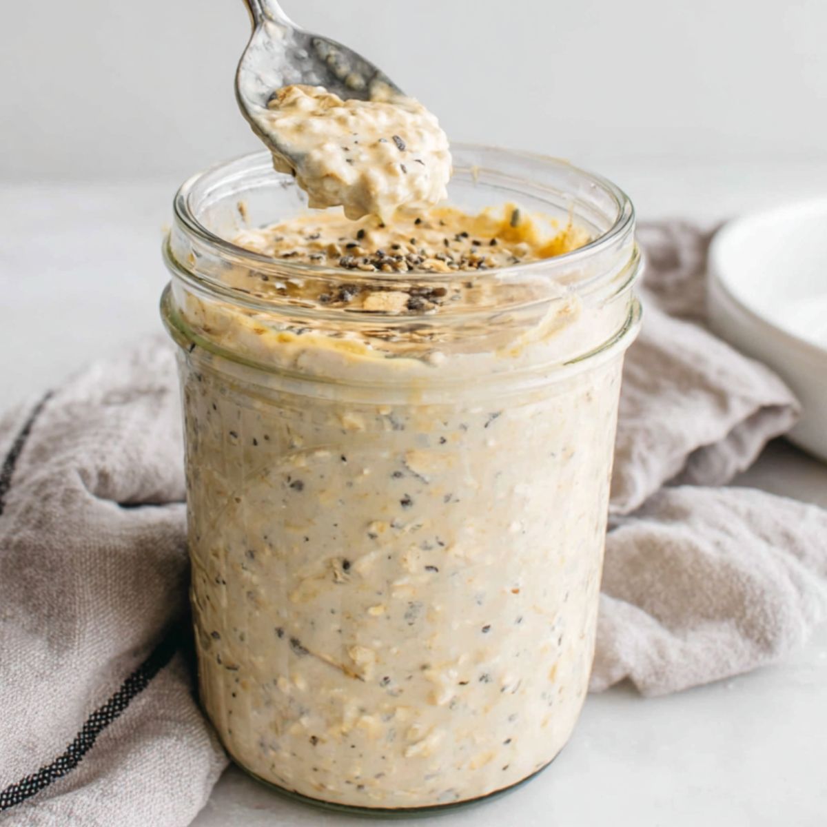 Stirring oats mixture before sealing jars for the fridge, with other jars nearby.