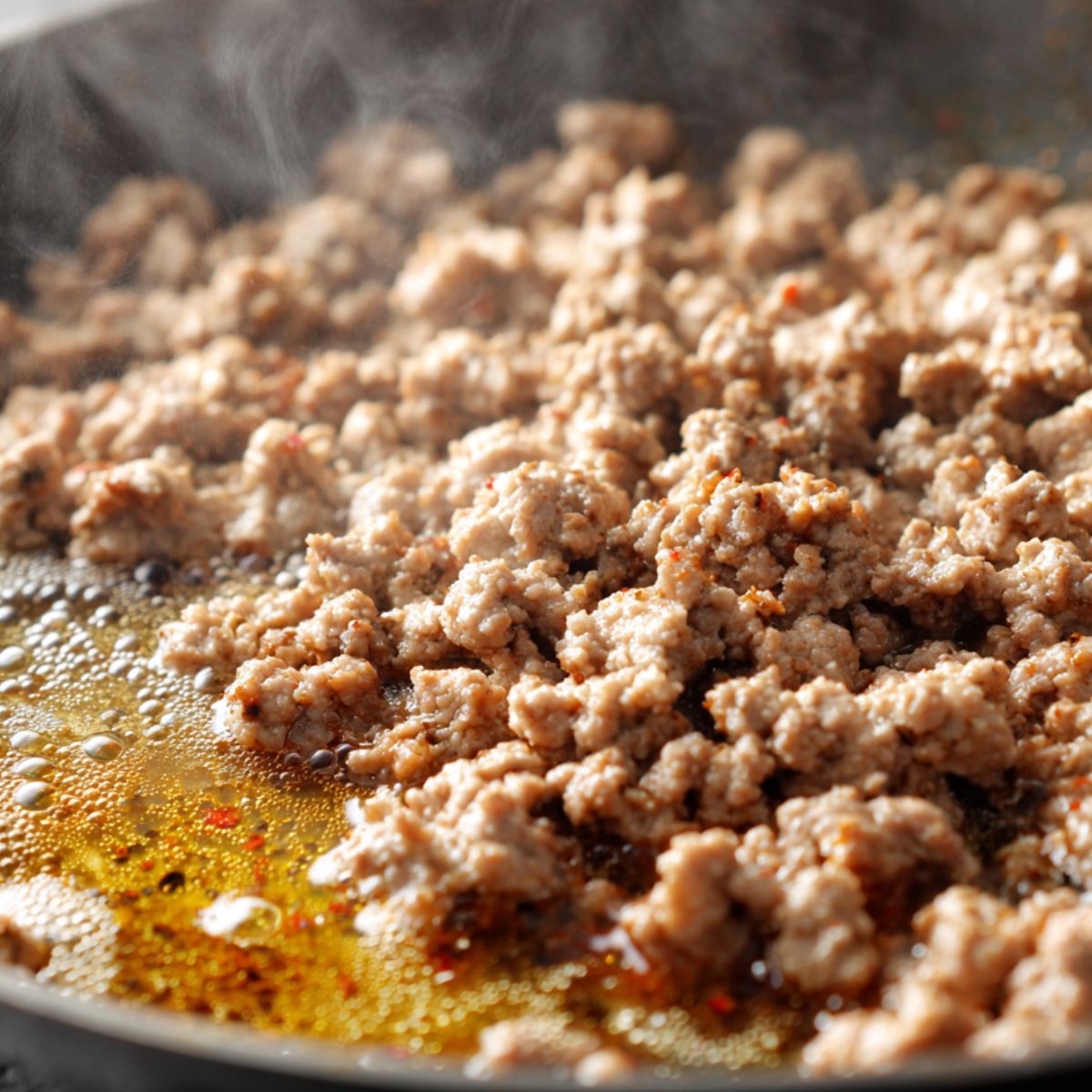 Ground pork browning in a skillet with garlic and ginger being added