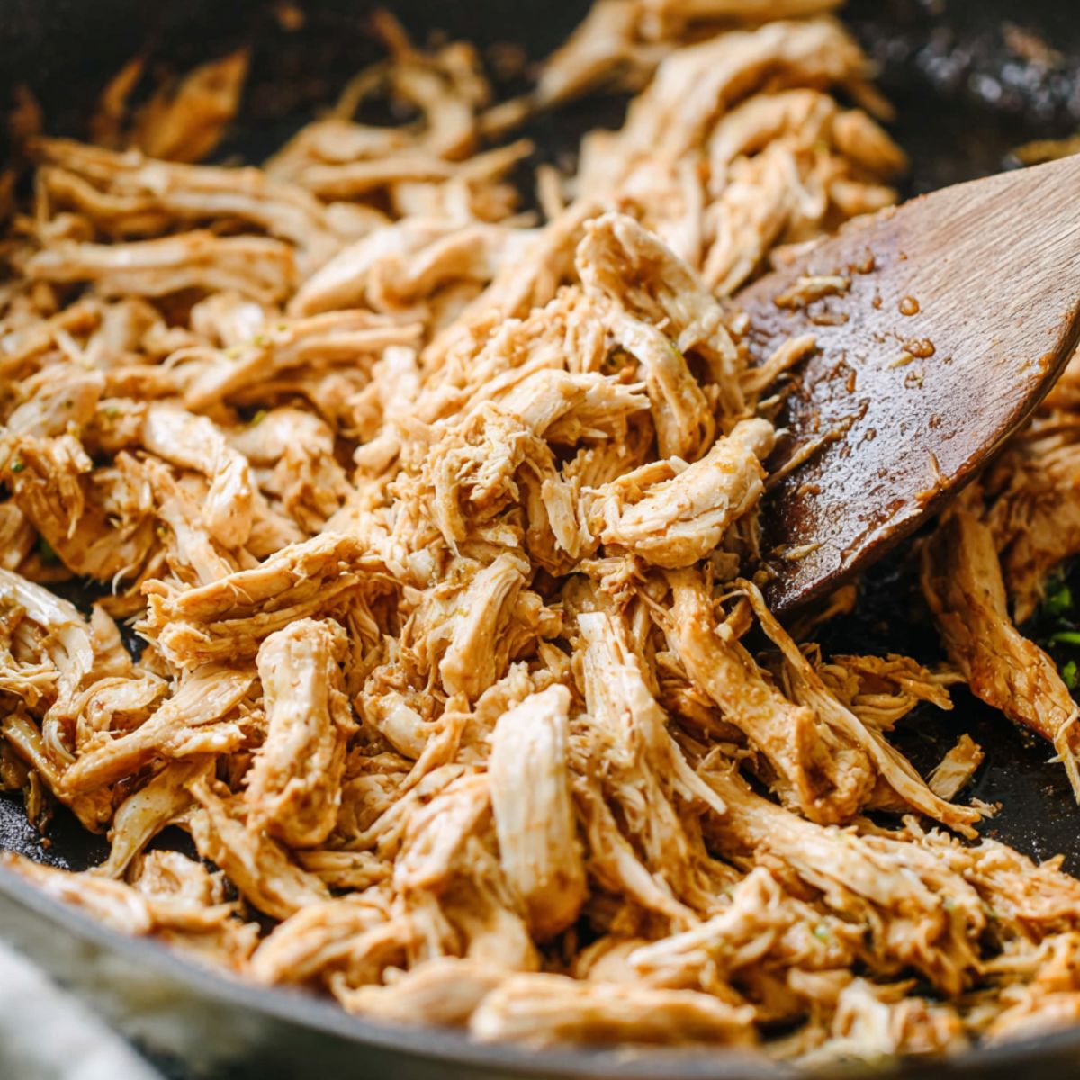Shredded chicken cooking in a skillet for wrap filling