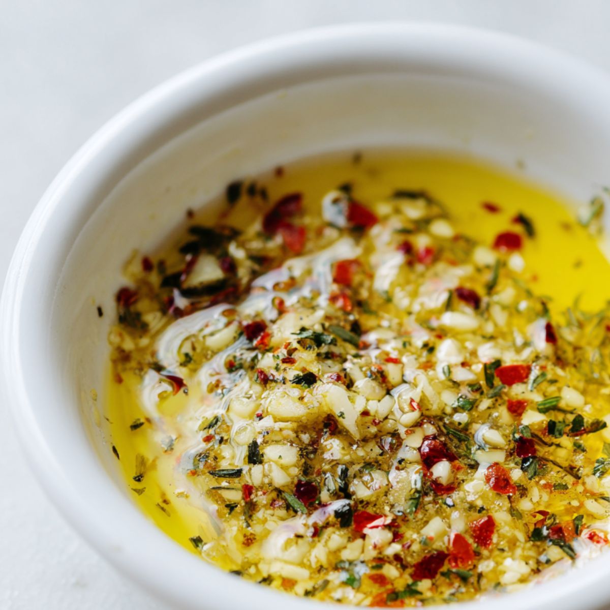 Melted garlic butter being mixed in a small bowl with herbs on the counter