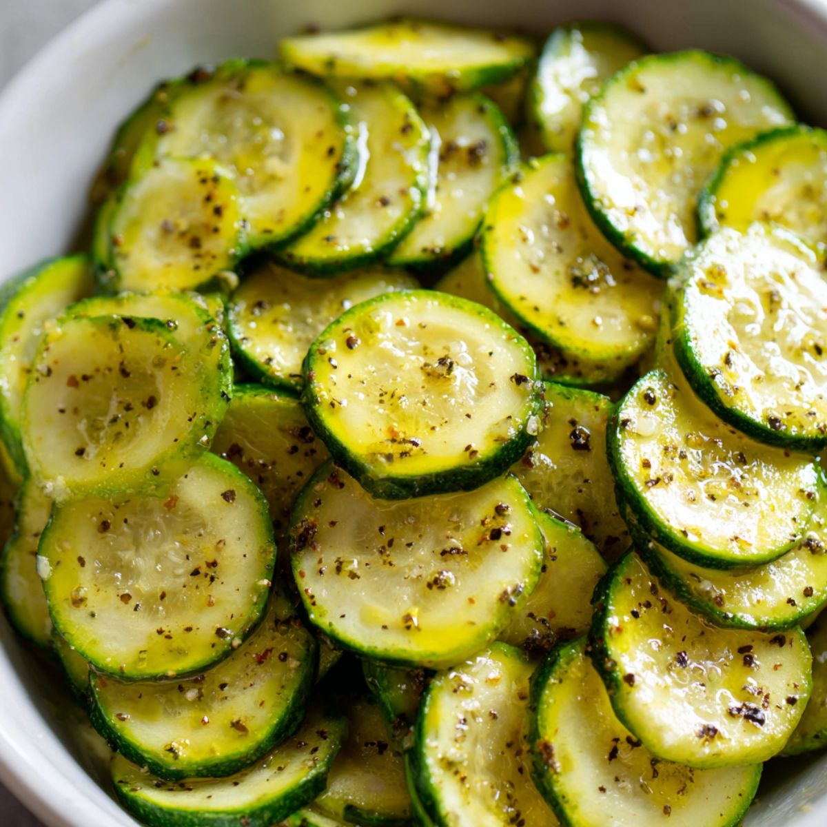 Zucchini slices tossed in oil and seasonings in a mixing bowl