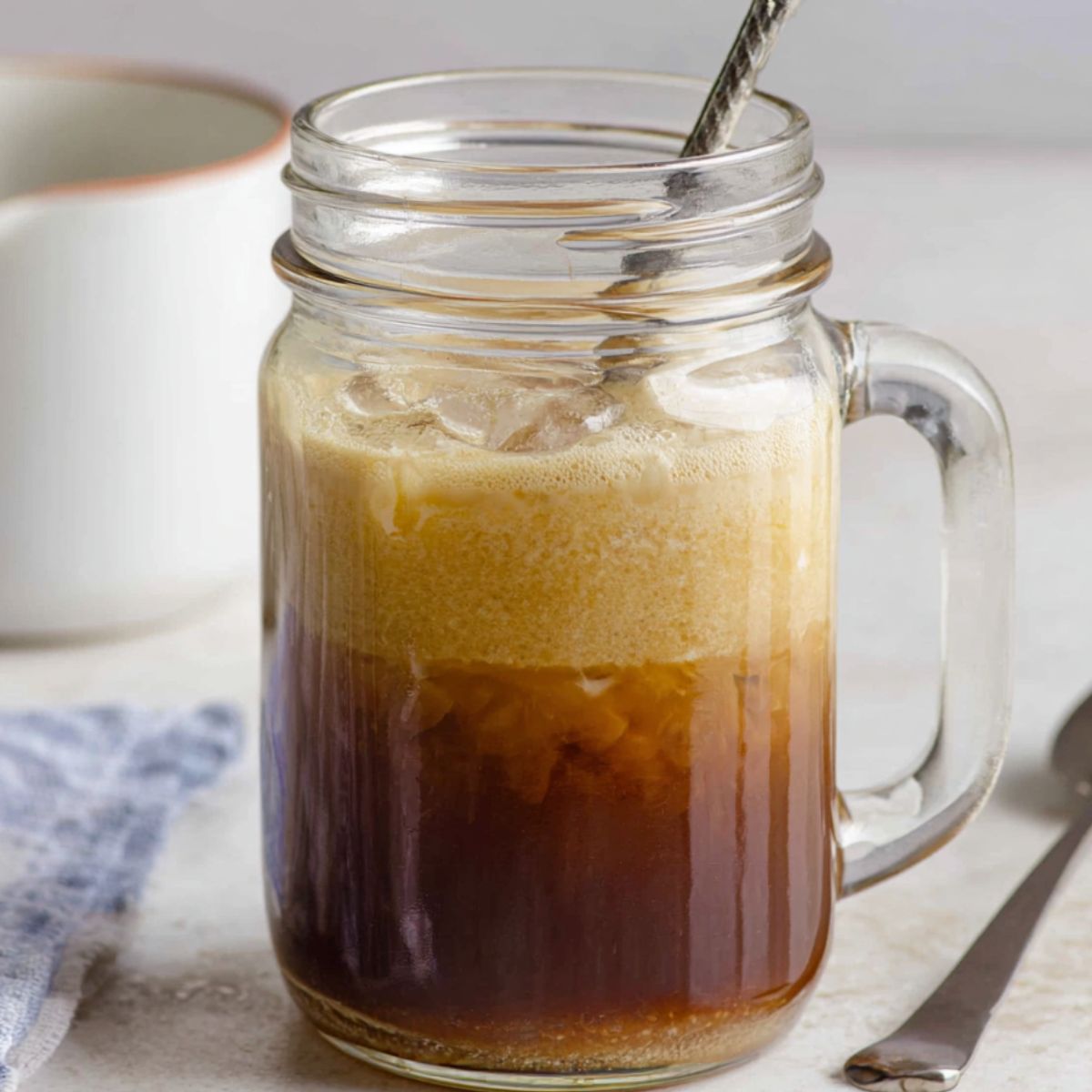 Shaking espresso and ice in a mason jar on a kitchen counter.