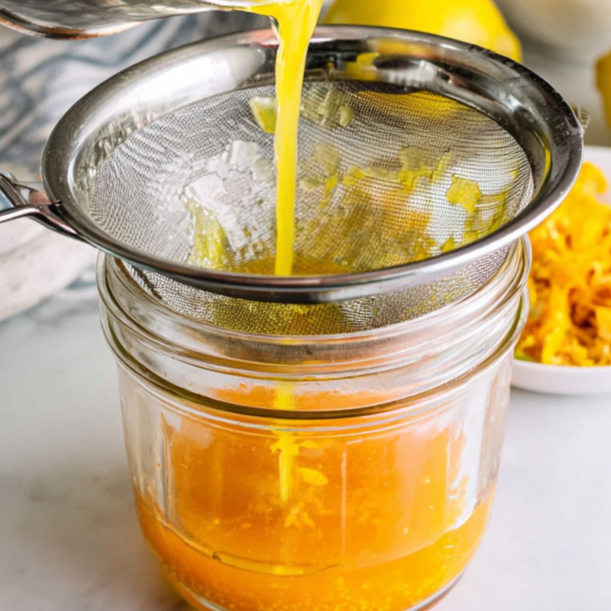 Filtering orange juice with lemon juice and zest nearby
