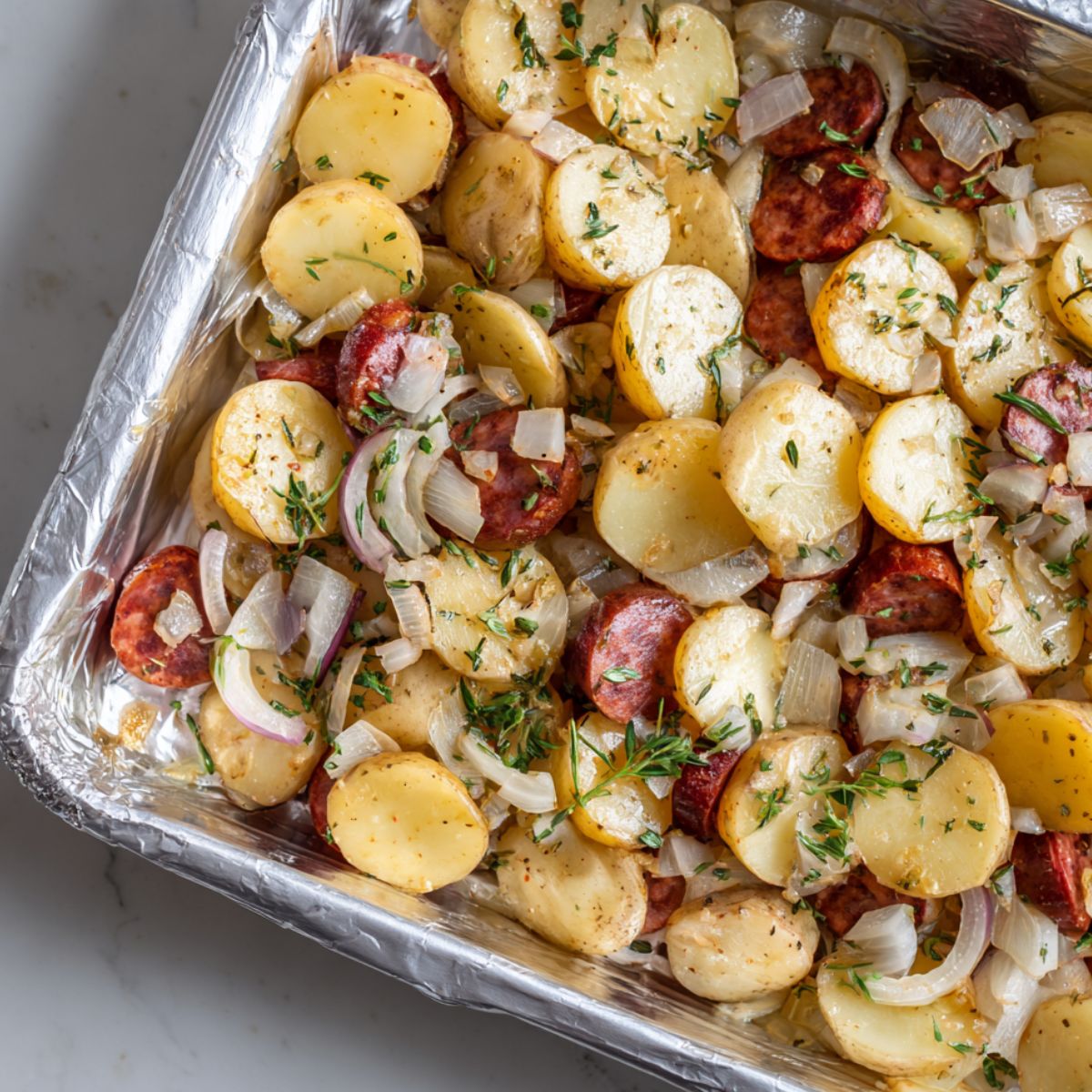 Potatoes and sausage layered in a baking dish before baking