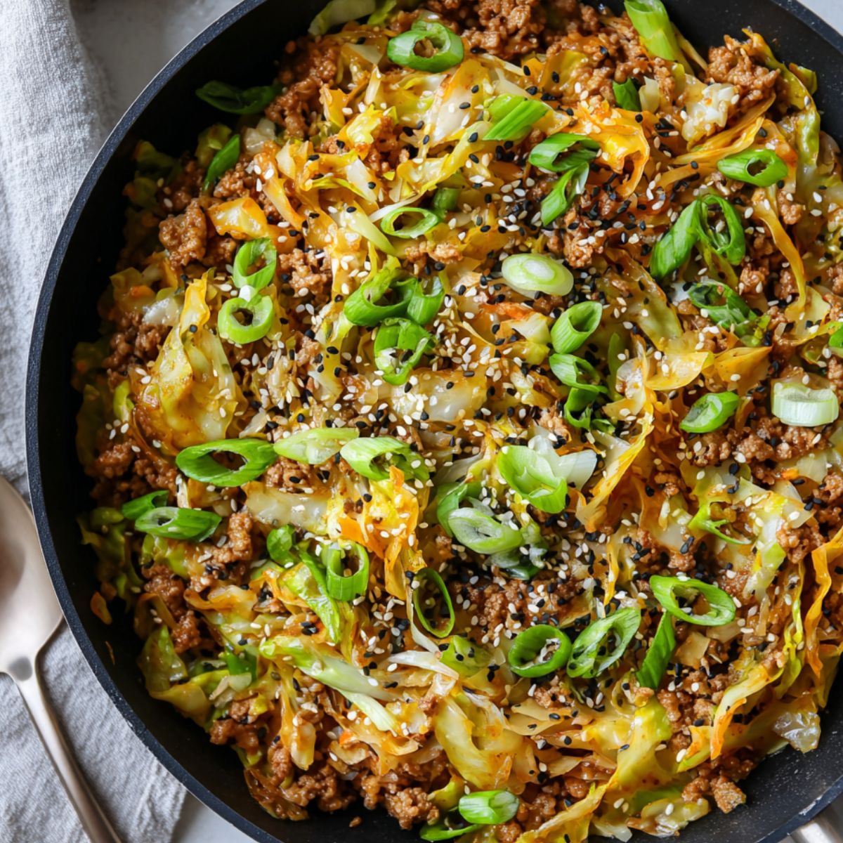 Finished keto egg roll in a bowl in a skillet garnished with green onions and sesame seeds