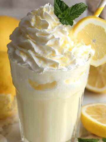 Overhead shot of whipped lemonade served in a glass with fluffy top, lemon slice, and mint on a white counter