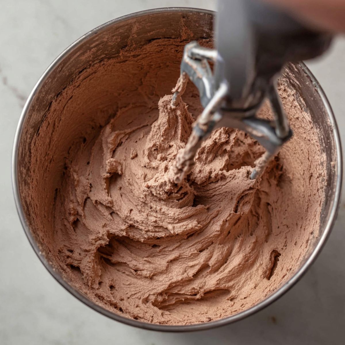 Whipping chocolate cream in a bowl using a hand mixer until stiff peaks form.