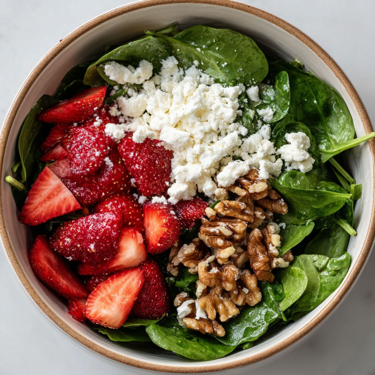 Overhead shot of a salad being assembled with spinach, strawberries, walnuts, and cheese.