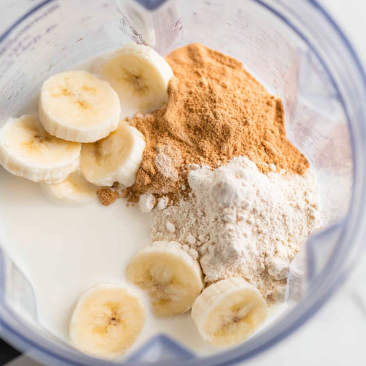 Adding bananas, almond milk, and protein powder to a blender for the best banana protein shake.