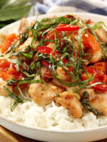 Creamy Thai basil chicken served over jasmine rice with basil leaves and chili on top, on a white kitchen counter.